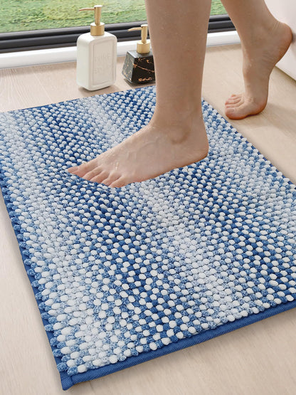 Blue textured bath mat with a foot stepping onto it, near a window.