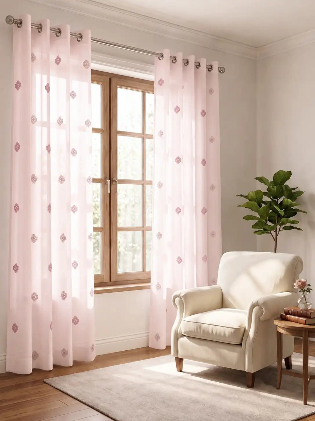 Light pink sheer grommet curtains with a small pink diamond pattern, hanging on a silver rod over a window in a bright, modern room with a cream armchair and a potted plant.